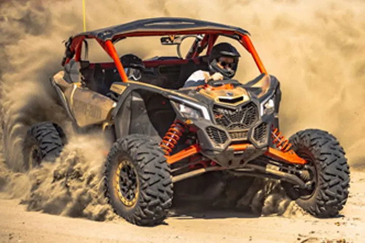 Man riding a Can-Am buggy, with clouds of dust trailing behind him in the desert