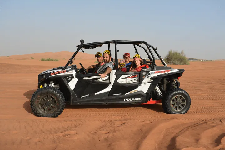 Family of five driving a black and white Polaris dune buggy through the Dubai desert