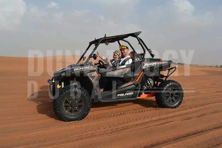 A couple enjoying a thrilling black Polaris RZR 1000 buggy ride in the dubai desert