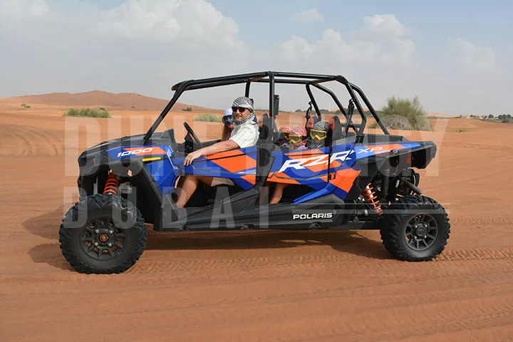 Man and family riding a blue Polaris RZR XP Pro dune buggy through Dubai desert with cloudy sky.