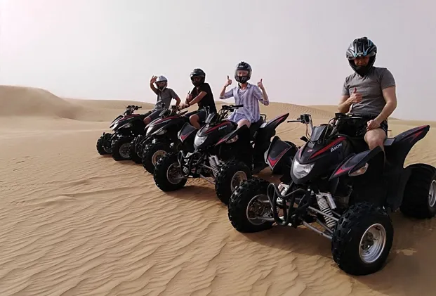 Four friends joyfully riding Kymco ATVs through the stunning desert landscape of Dubai.